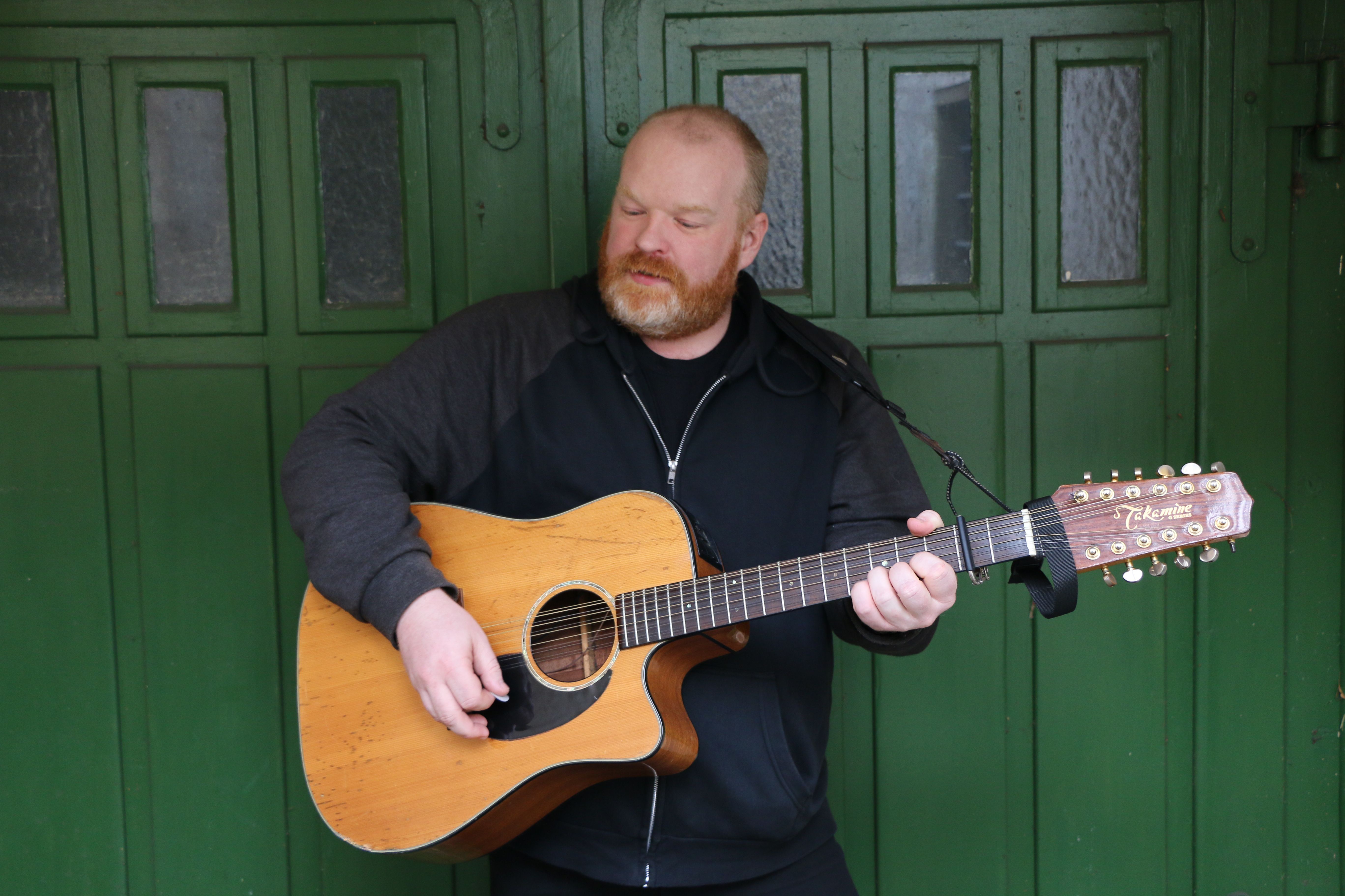 Mann mit Gitarre vor grünem Fenster