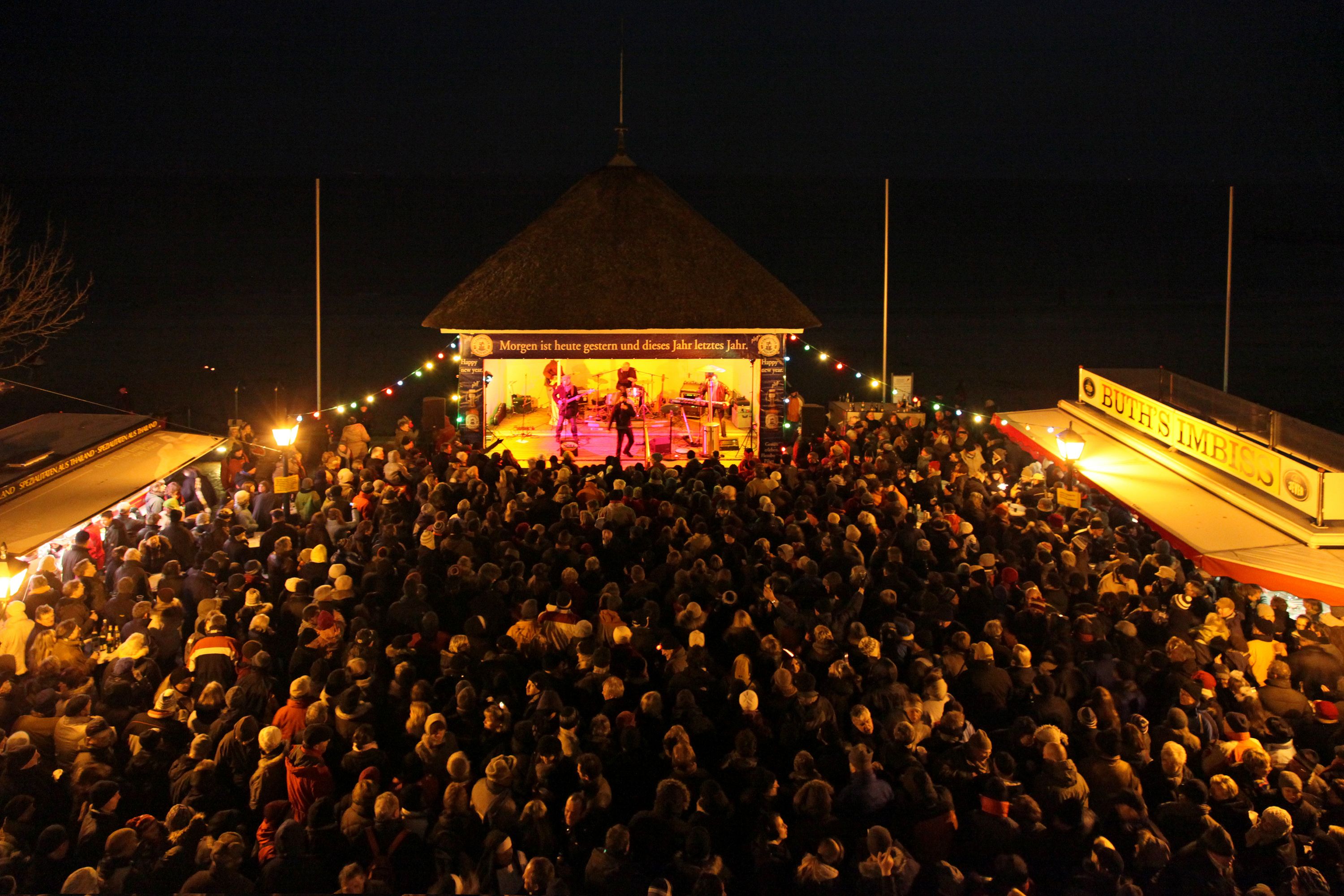 Feiernde Menschen tanzen vor einem beleuchteten Musikpavillon auf einer Open-Air-Silvesterparty