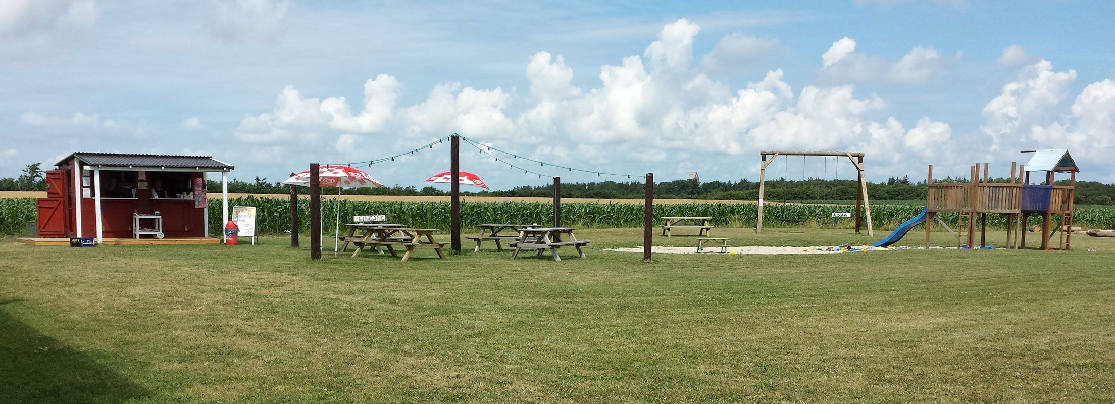 Der Eingang Labyrinth. Ein Kioskhäuschen, Sitzgelegenheiten und ein Spielplatz. Beim Föhrer Maislabyrinth auf Föhr