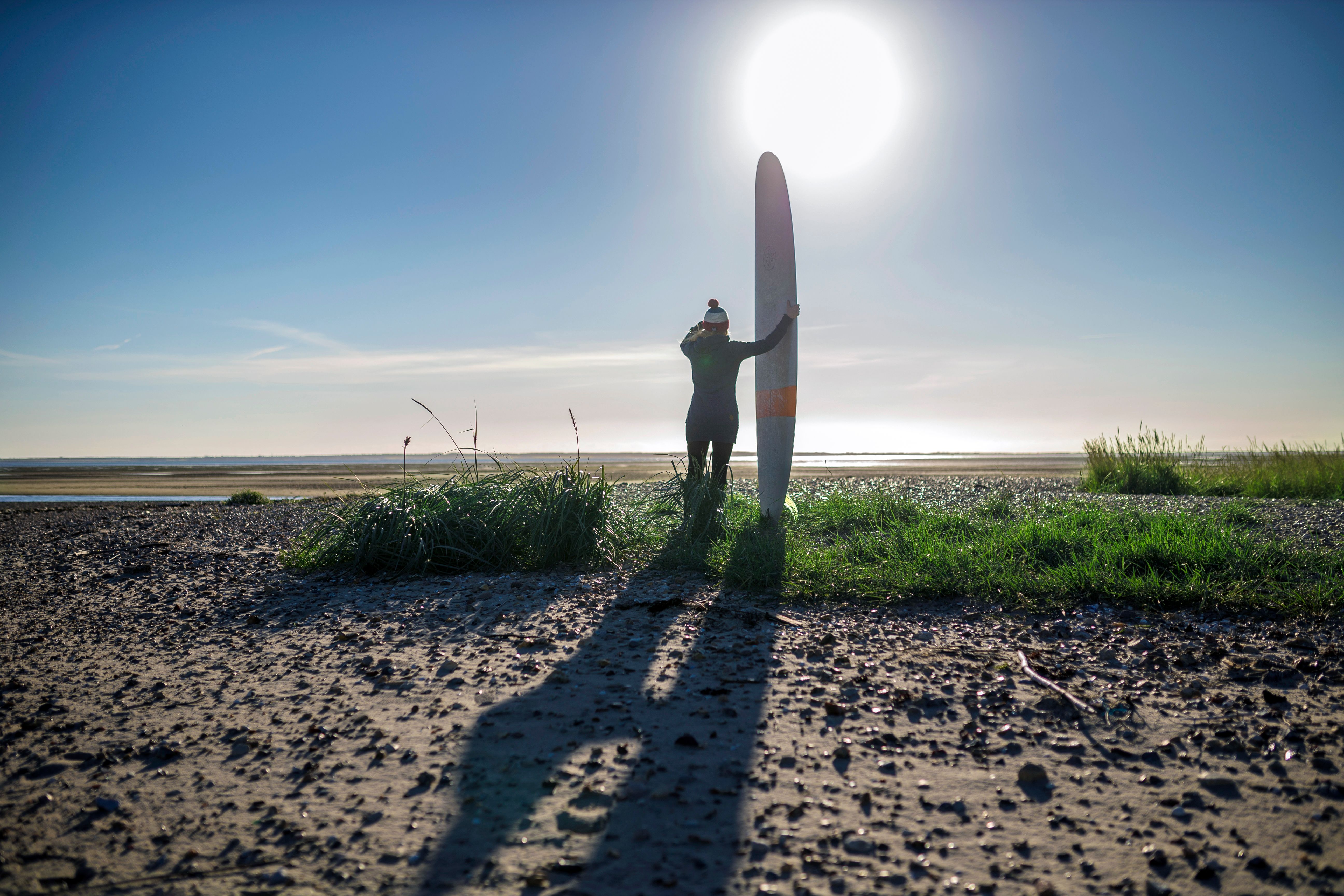 Person von hinten mit einem Surfbrett in der Hand